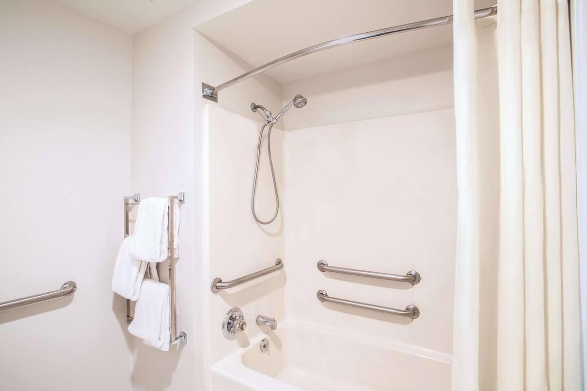 Une salle de bain équipée d’une baignoire, de barres d’appui et d’un pommeau de douche.