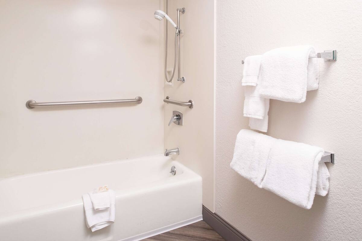 Une salle de bain équipée d’une baignoire, de barres d’appui, d’un pommeau de douche et de plusieurs serviettes blanches disposées sur un porte-serviettes.