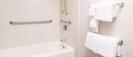 A bathroom with a bathtub, grab bars, a showerhead, and multiple white towels on a rack.