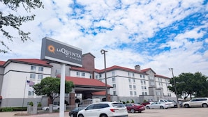 Un hotel con un cartel que dice "LA QUINTA BY WYNDHAM", que cuenta con un estacionamiento con varios autos y un cielo despejado.