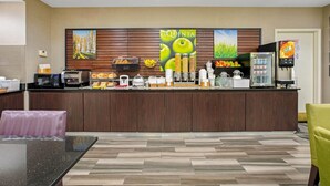 Zona de recepción de hotel con mostrador, máquinas de café y refrigerador.