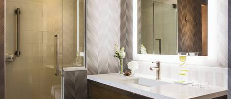 Une salle de bain moderne avec une douche à l’italienne en verre, un lavabo blanc avec un meuble-vasque en bois, et un grand miroir au-dessus du lavabo.