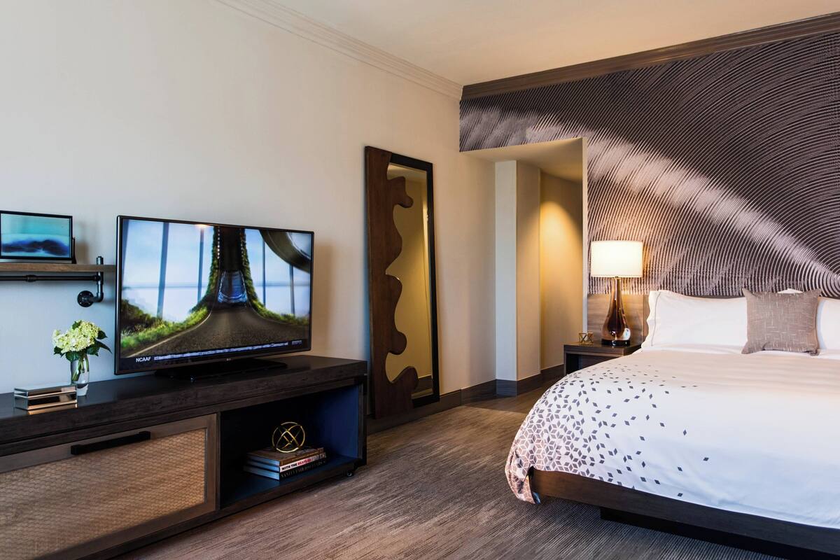 Hotellihuone, jossa on suuri sänky, taulutelevisio, yöpöytä ja seinälle kiinnitetty peili.