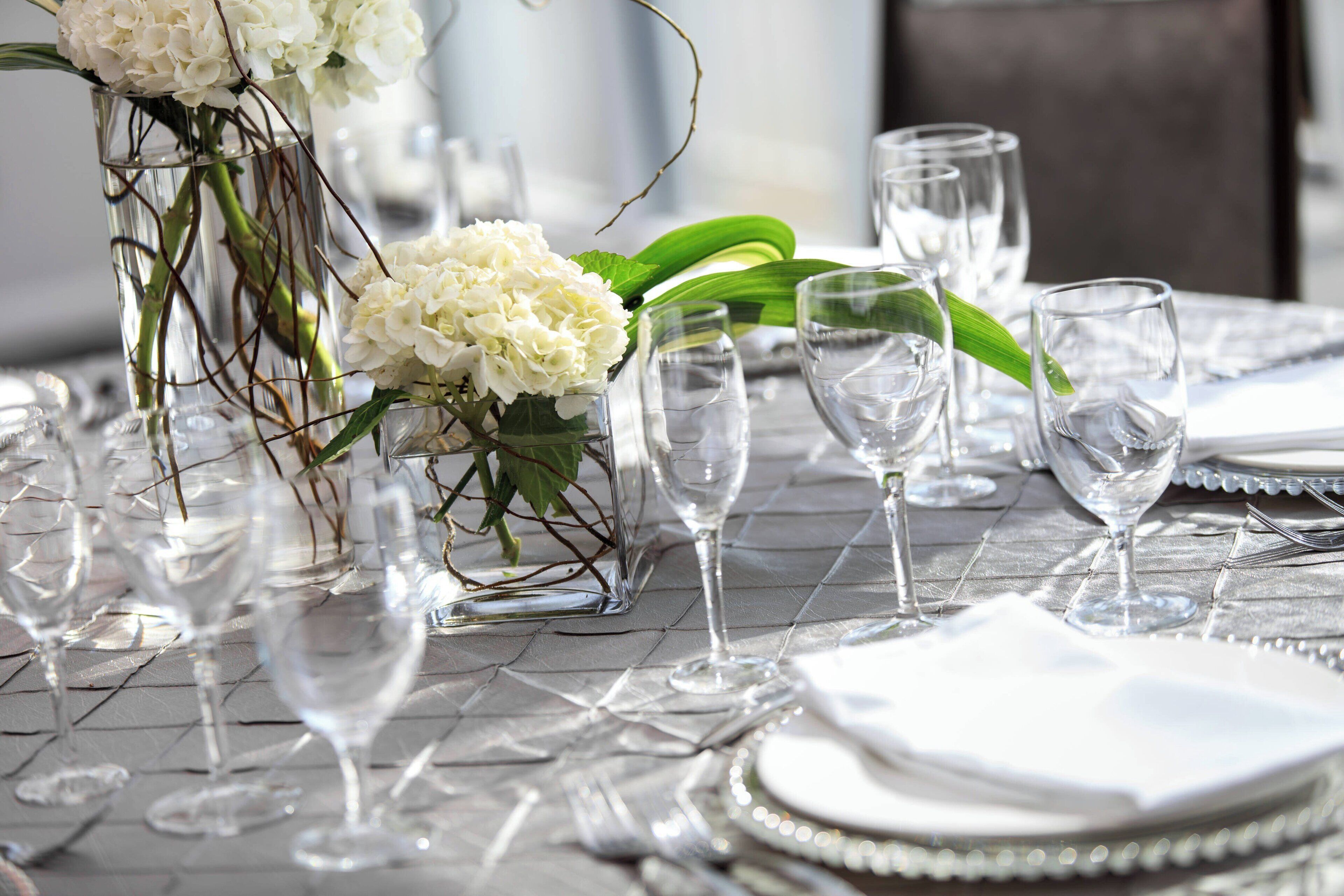 A table set with clear glassware, white napkins, and white flowers in a vase.