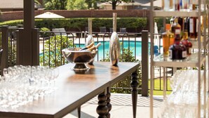 Ein Barbereich am Pool mit einem langen Tisch, der mit Gläsern und Flaschen, einer Schüssel für Besteck und einer dekorativen Vase gedeckt ist.