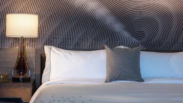 A neatly made bed with white and gray bedding, a modern lamp on a wooden nightstand, and a textured wall behind the bed.