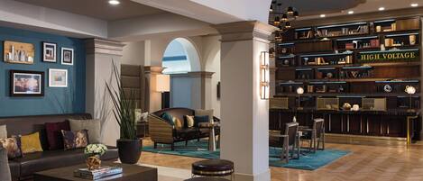 A spacious living area with a sofa, coffee table, and bar seating. A bookshelf labeled "HIGH VOLTAGE" is visible.