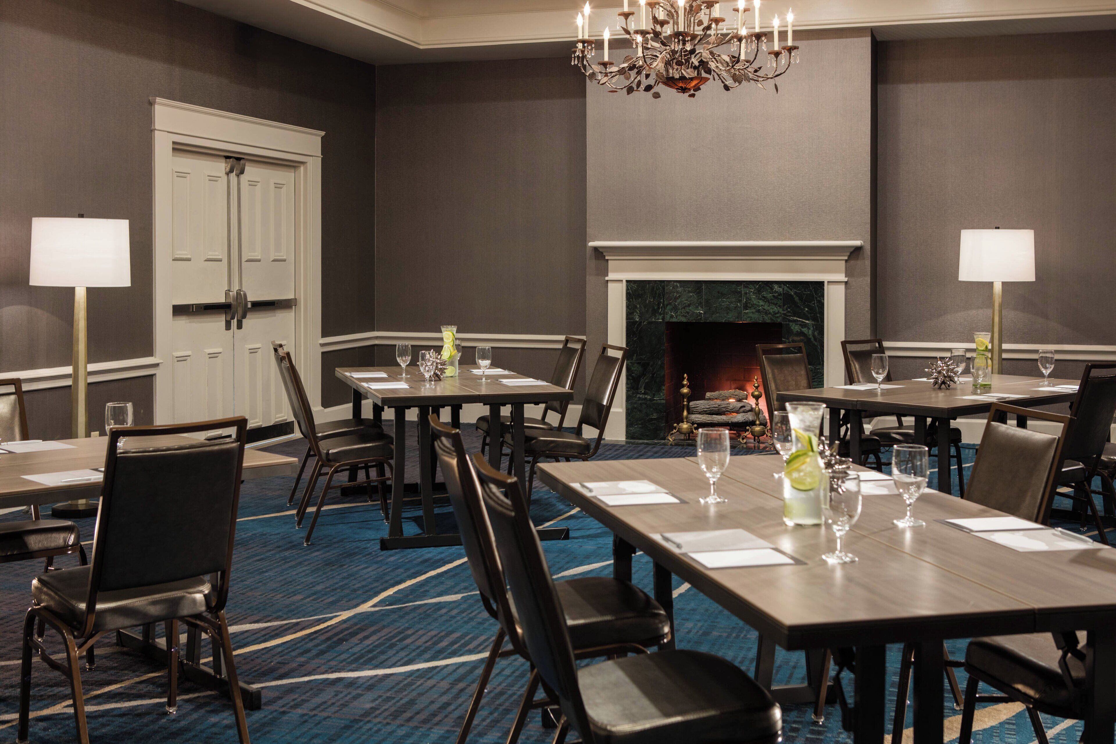 A conference room with multiple tables and chairs, a fireplace, and chandeliers.