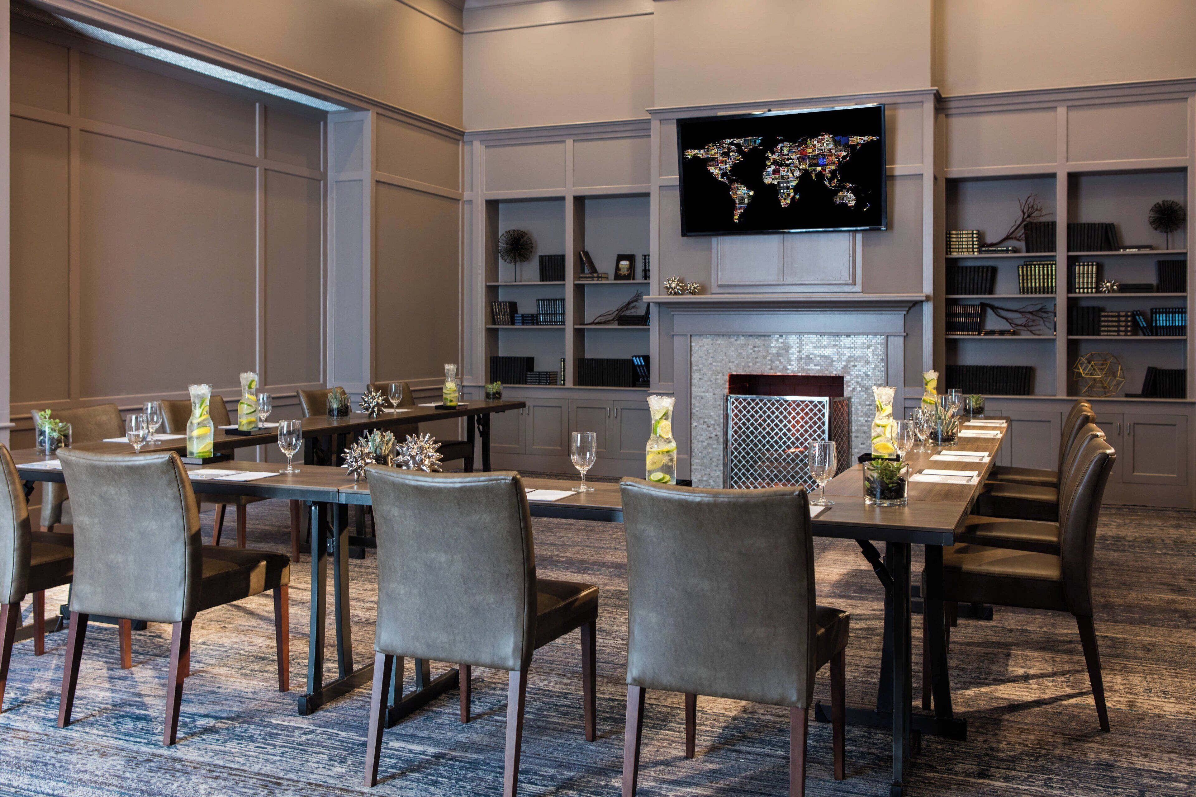 A conference room with a long table, chairs, a television mounted on the wall, and bookshelves.