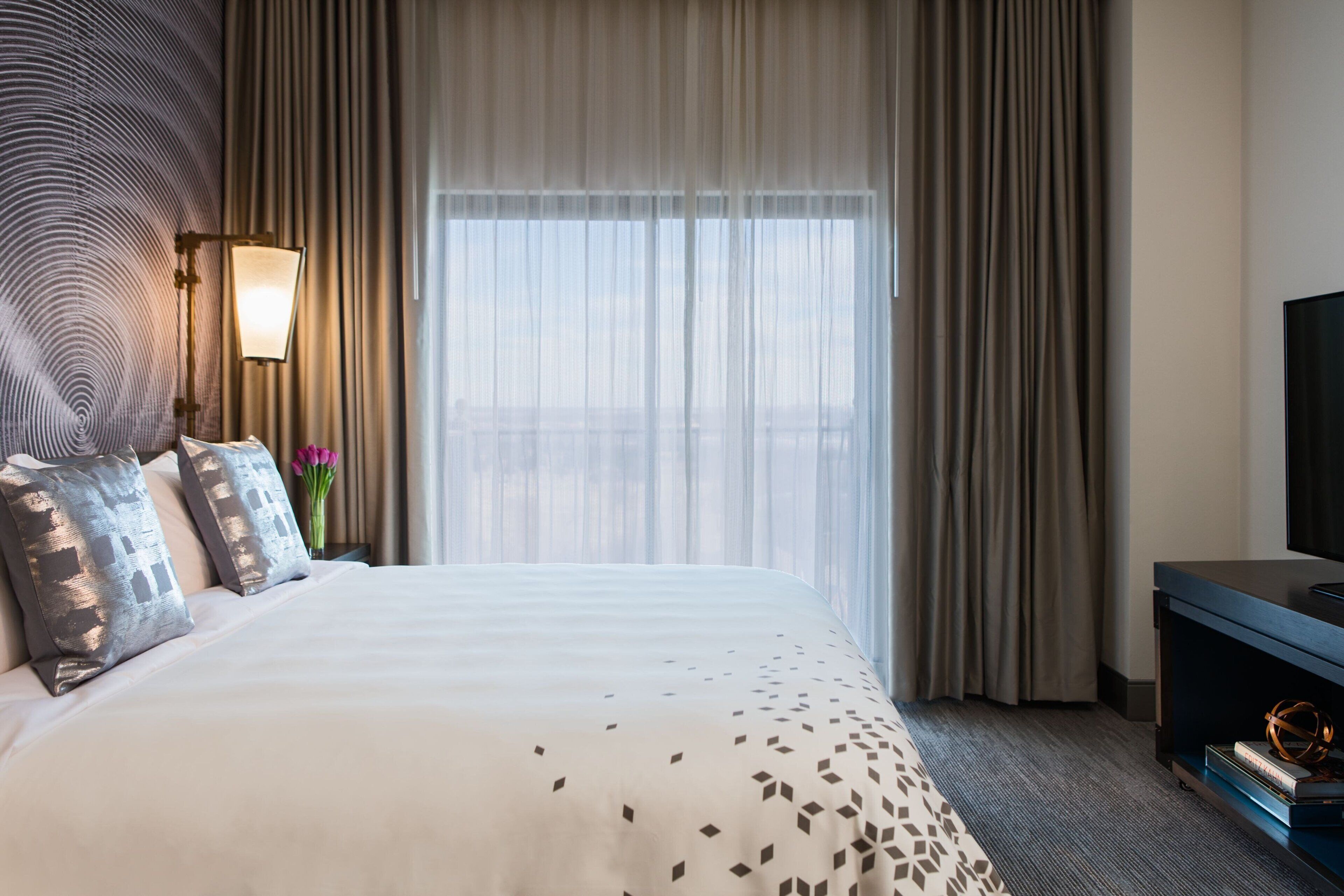 A hotel room with a large bed, a TV, and a window with curtains.