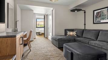 A modern living room with a sectional sofa, a desk with a chair, and a large window providing a view of the outdoors.