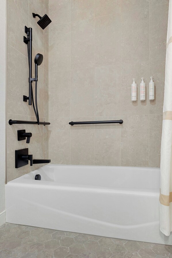 A modern bathroom with a bathtub, shower, and handrails.