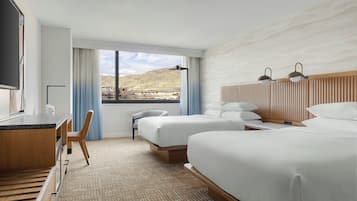 A hotel room with a bed, a desk, a chair, a TV, and a view of the mountains.