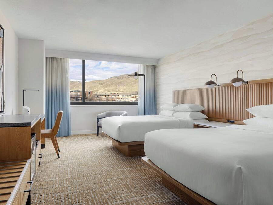 A hotel room with a bed, a desk, a chair, a TV, and a view of the mountains.