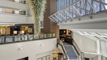 A multi-level hotel lobby with a central staircase, a hanging plant installation, and a modern glass ceiling structure.