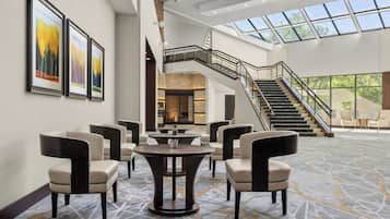 A spacious lobby with a high ceiling, a staircase, and a seating area with round tables and chairs.