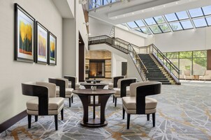 A spacious lobby with a high ceiling, a staircase, and a seating area with round tables and chairs.