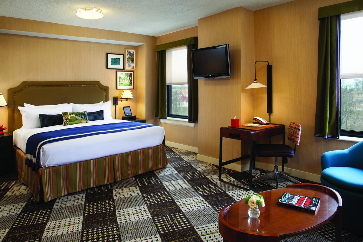 A hotel room with a bed, a desk, a chair, a television, and a window.