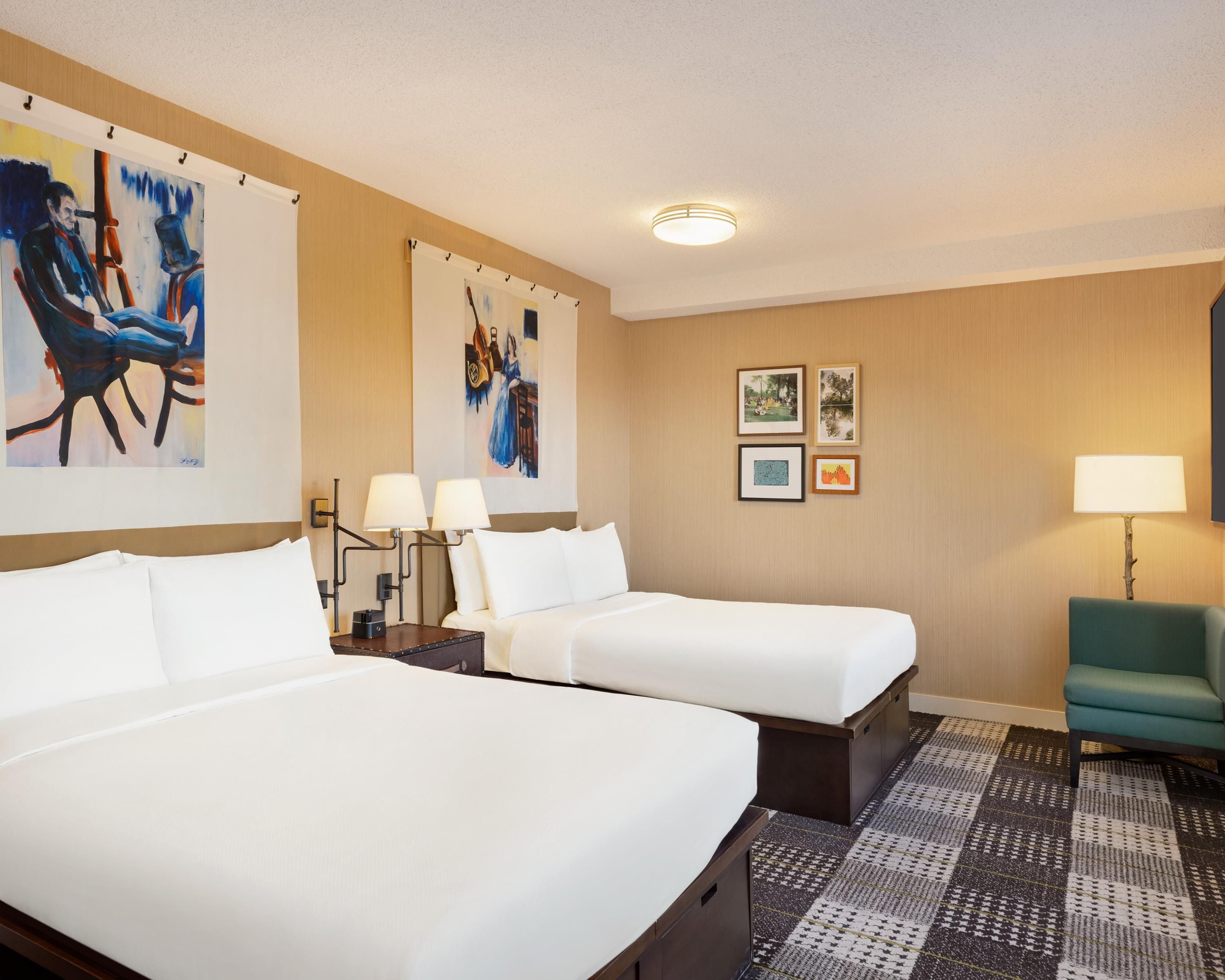 A hotel room with two beds, a desk, a chair, and artwork on the walls.