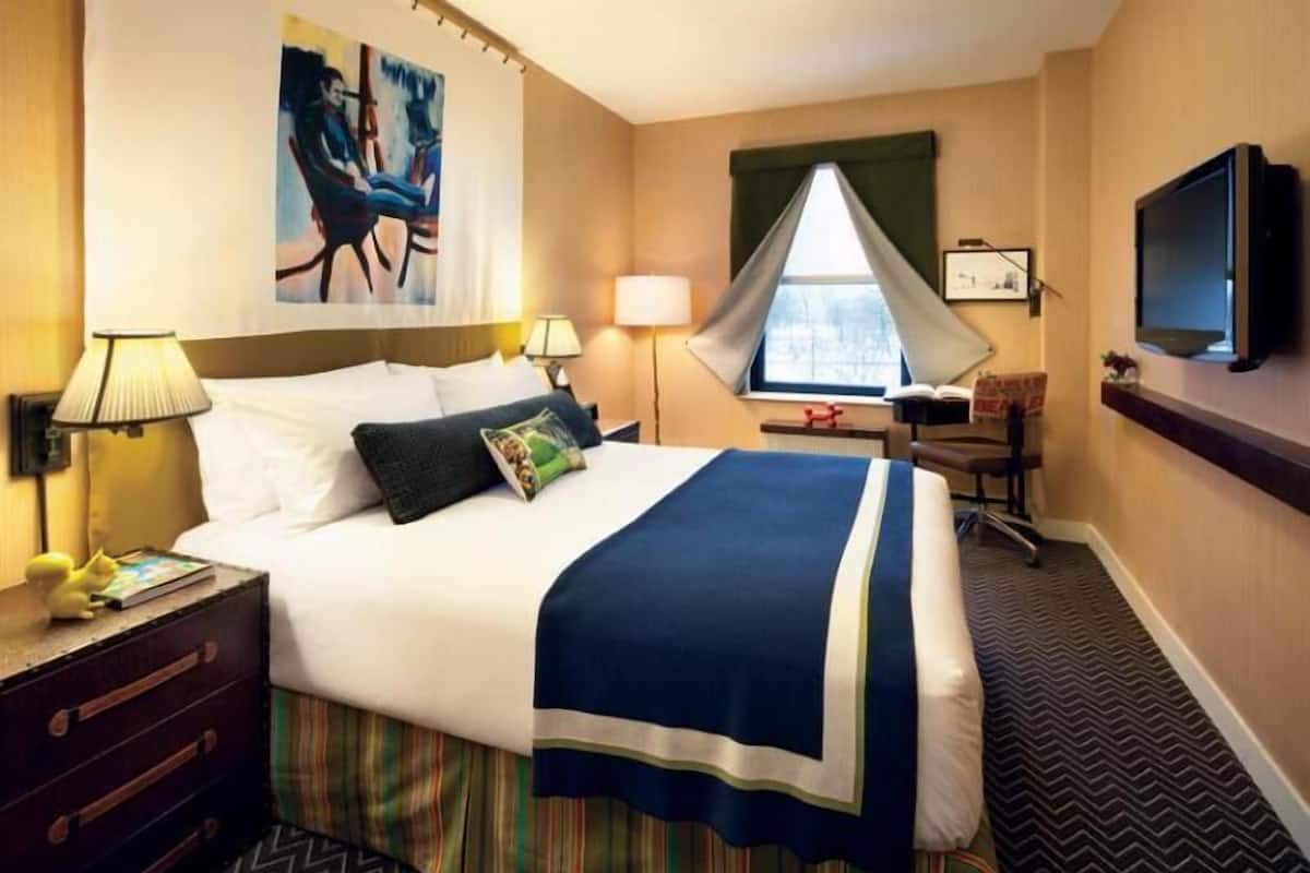 Una camera d'albergo con un letto, comodini, una scrivania, una sedia, una televisione e una finestra.