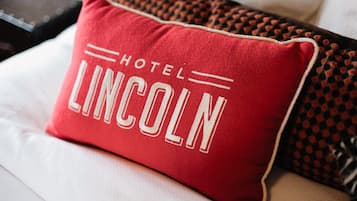 Un cojín rojo con el texto "HOTEL LINCOLN" sobre un sofá blanco.