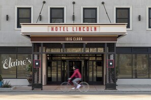The entrance of Hotel Lincoln with a clear sign above the doors and a cyclist passing by. - Hotel Lincoln (Chicago)