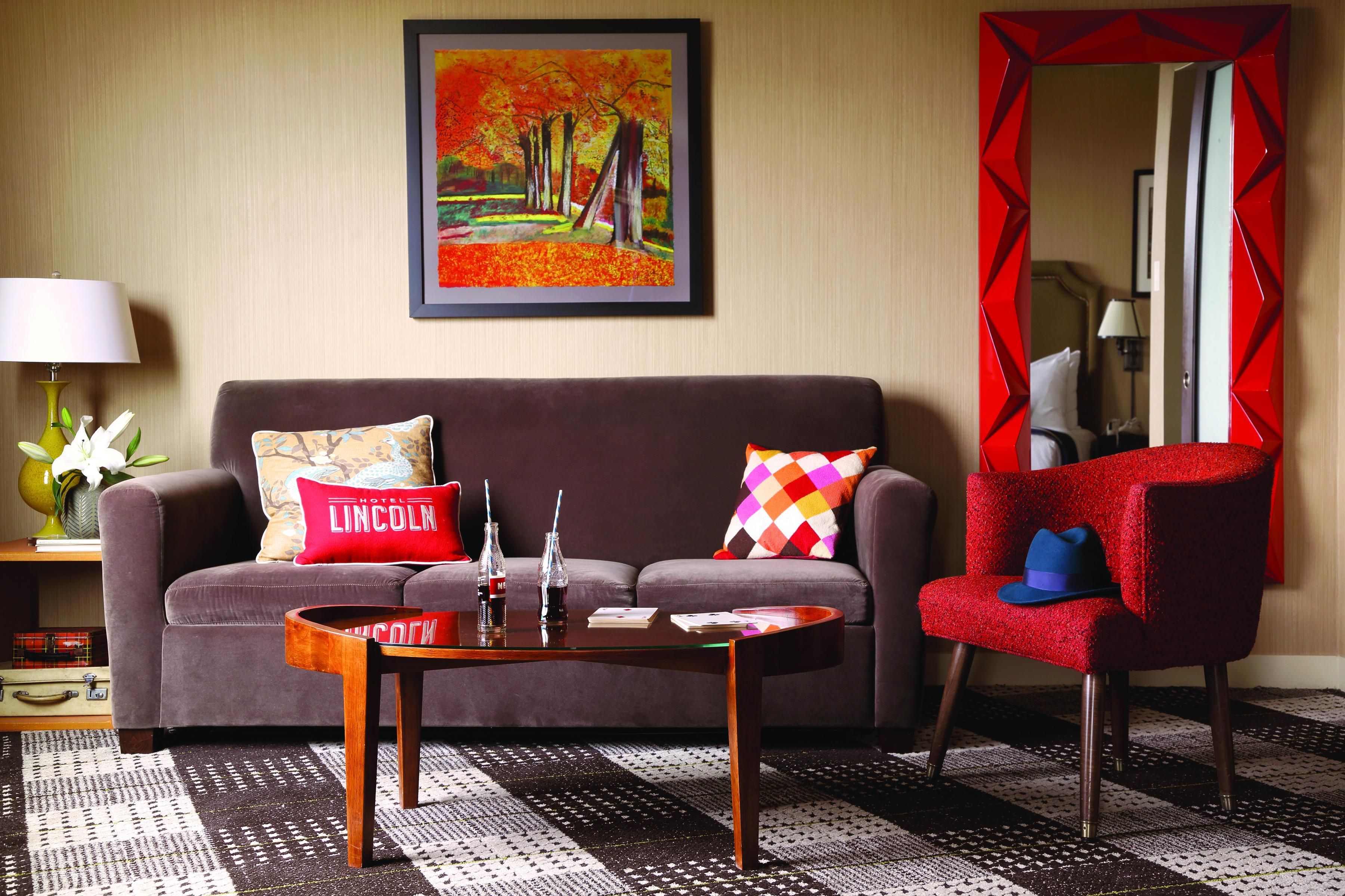 A hotel room with a brown sofa, a red armchair, a coffee table, and a framed painting on the wall.