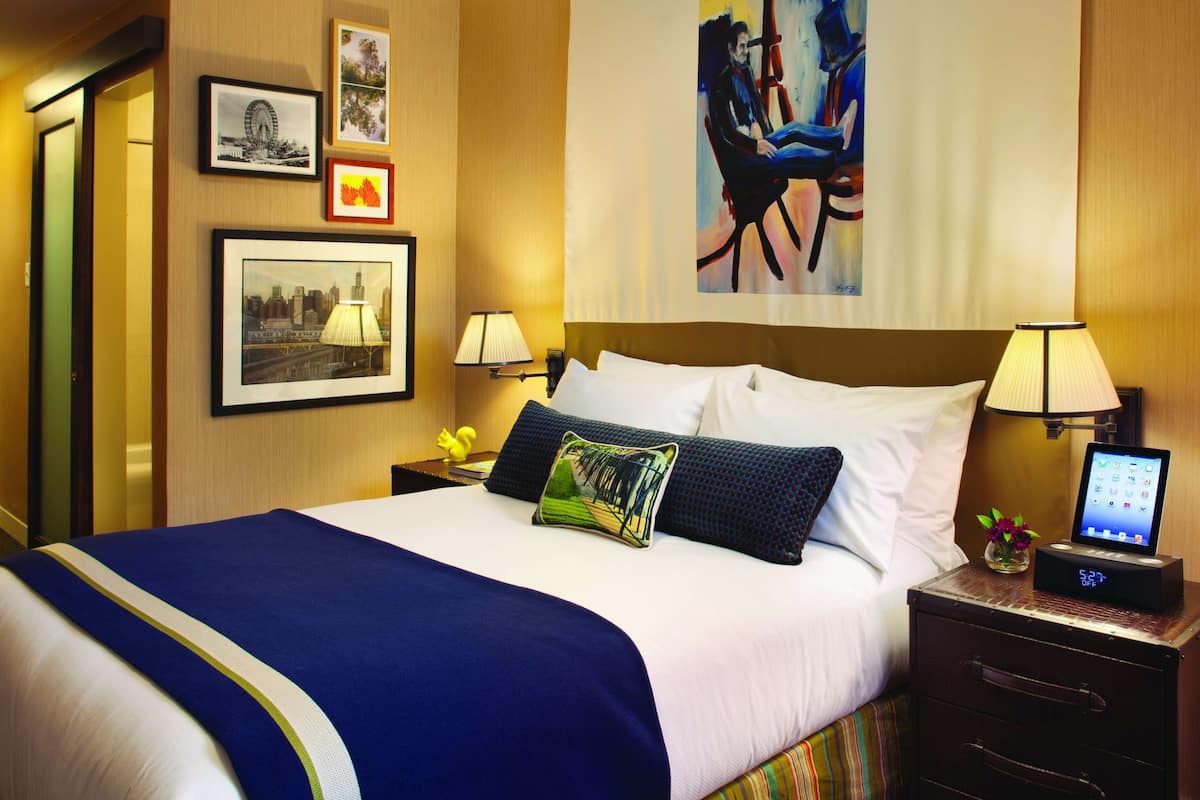 Una camera d'albergo con un letto grande, due comodini, un tavolino e una parete decorata con quadri e opere d'arte.