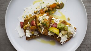 A white plate with a dish consisting of bread topped with cheese, vegetables, and a drizzle of olive oil. - Hotel Lincoln (Chicago)