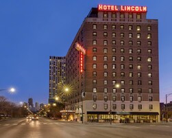 Un hotel de varios pisos con un llamativo letrero 'HOTEL LINCOLN', una fachada bien iluminada y una vista de la calle con coches estacionados.
