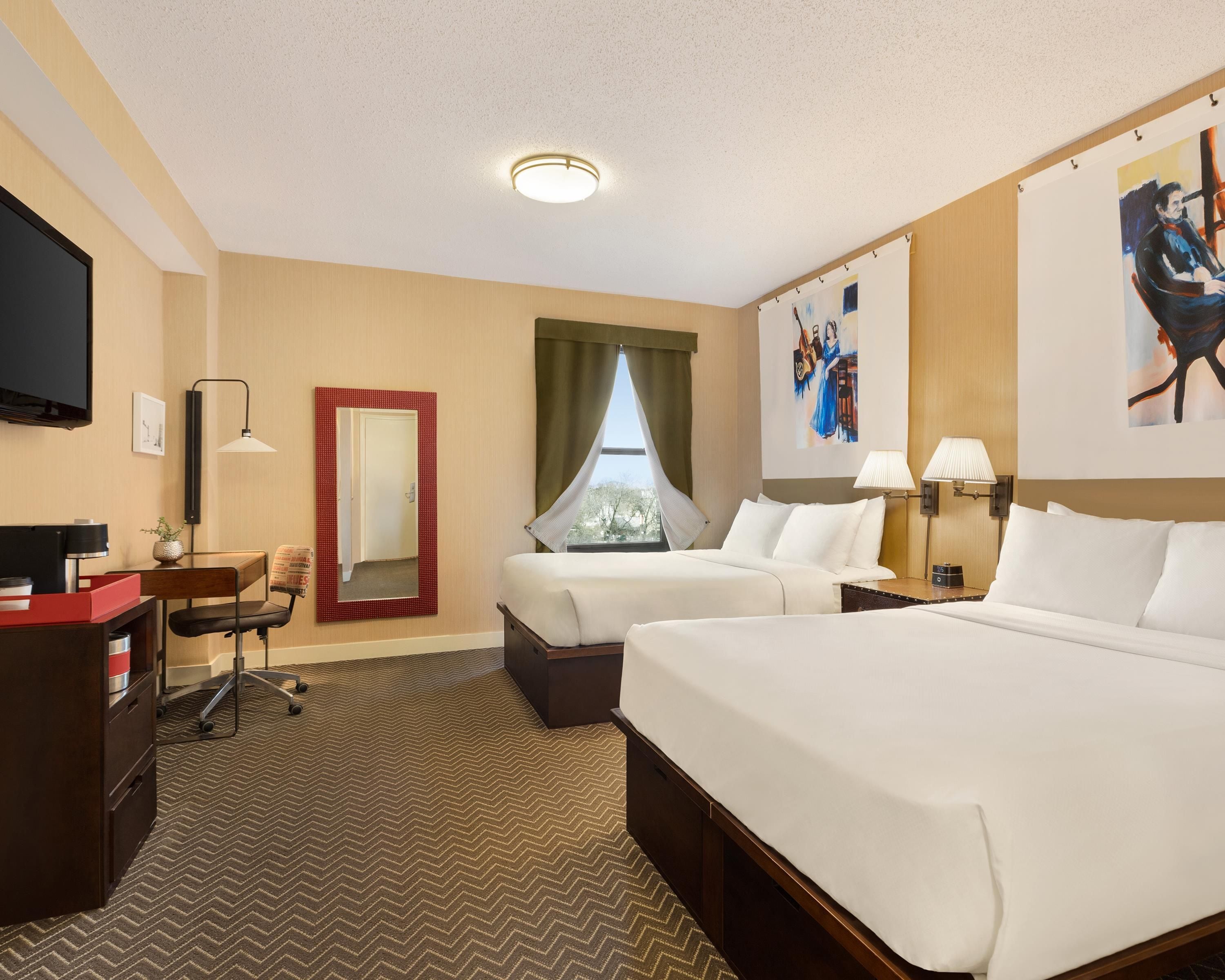 A hotel room with two beds, a desk, a chair, a TV, a painting, and a window with curtains.