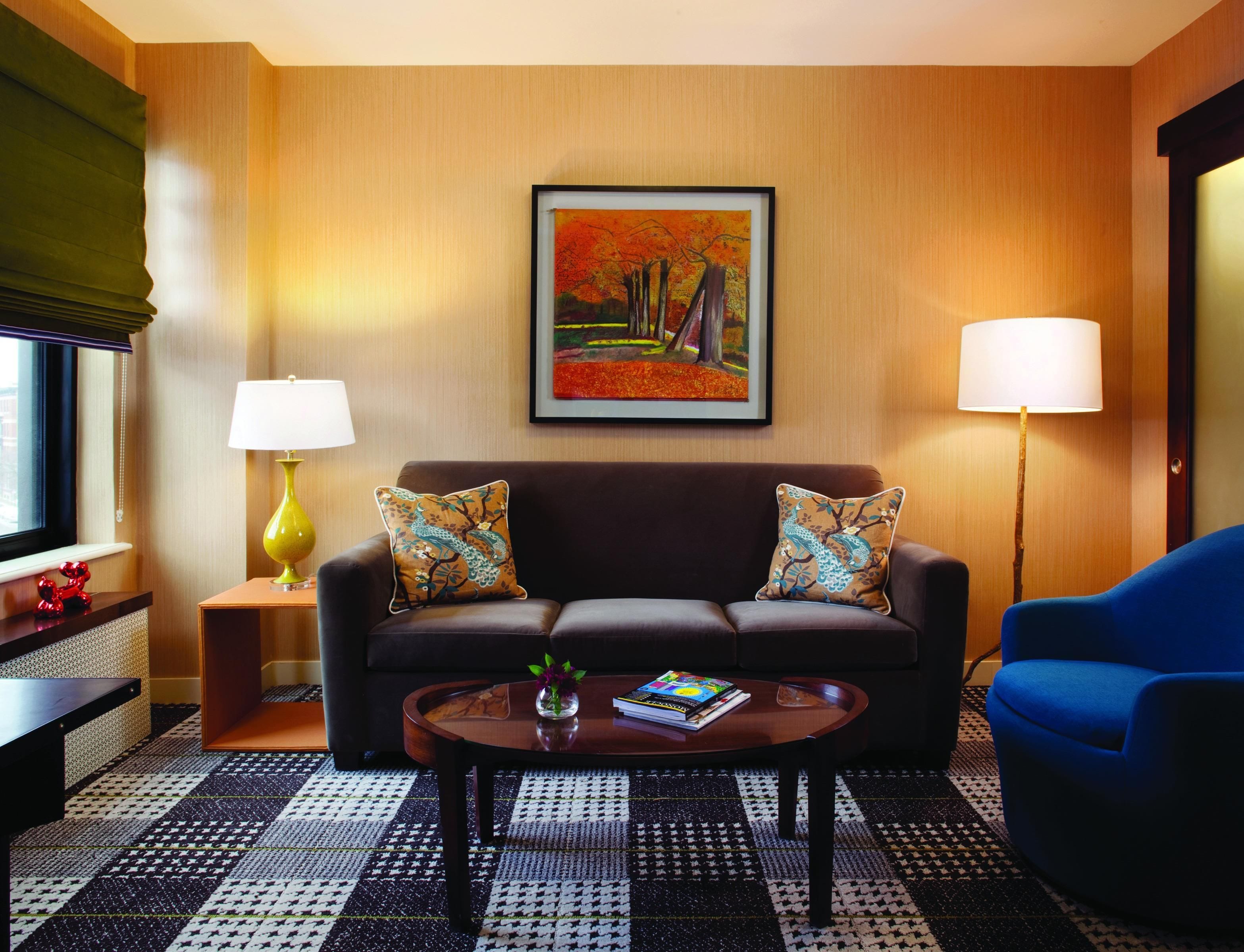 Habitación de hotel con sofá, un sillón azul, una mesa de centro, lámpara y un cuadro en la pared.