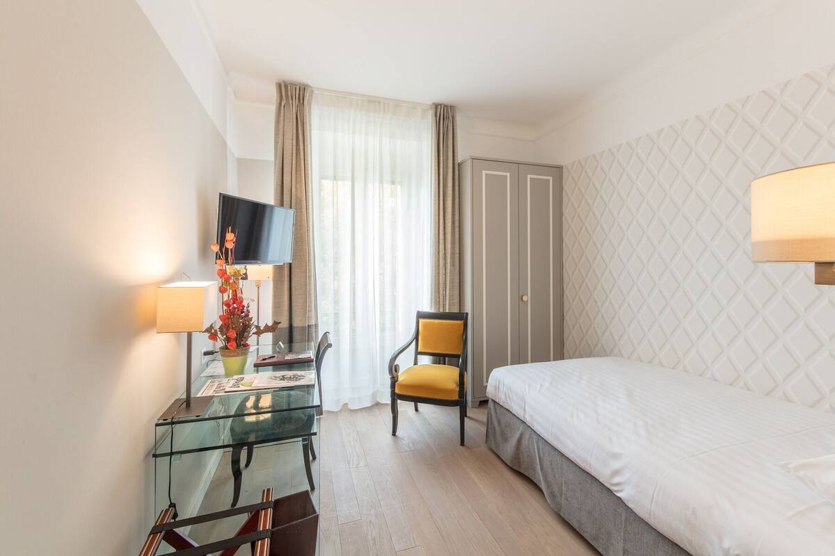 Una habitación de hotel con una cama, un escritorio con lámpara, una silla, un televisor y un armario.