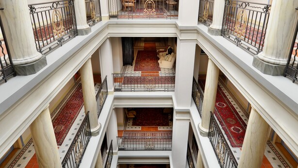 Een meerlaags atrium met marmeren kolommen, versierde leuningen en betegelde tapijten.