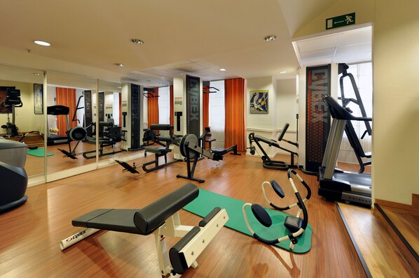 A gym with cardio machines, weight training equipment, and a mirrored wall.