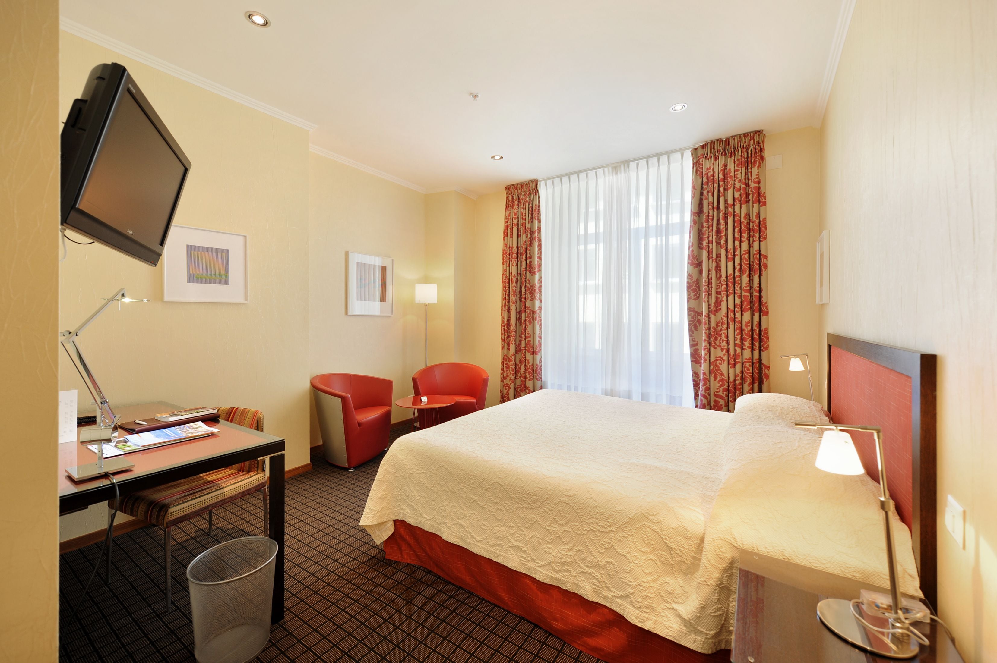A hotel room with a bed, desk, chair, TV, and curtains.