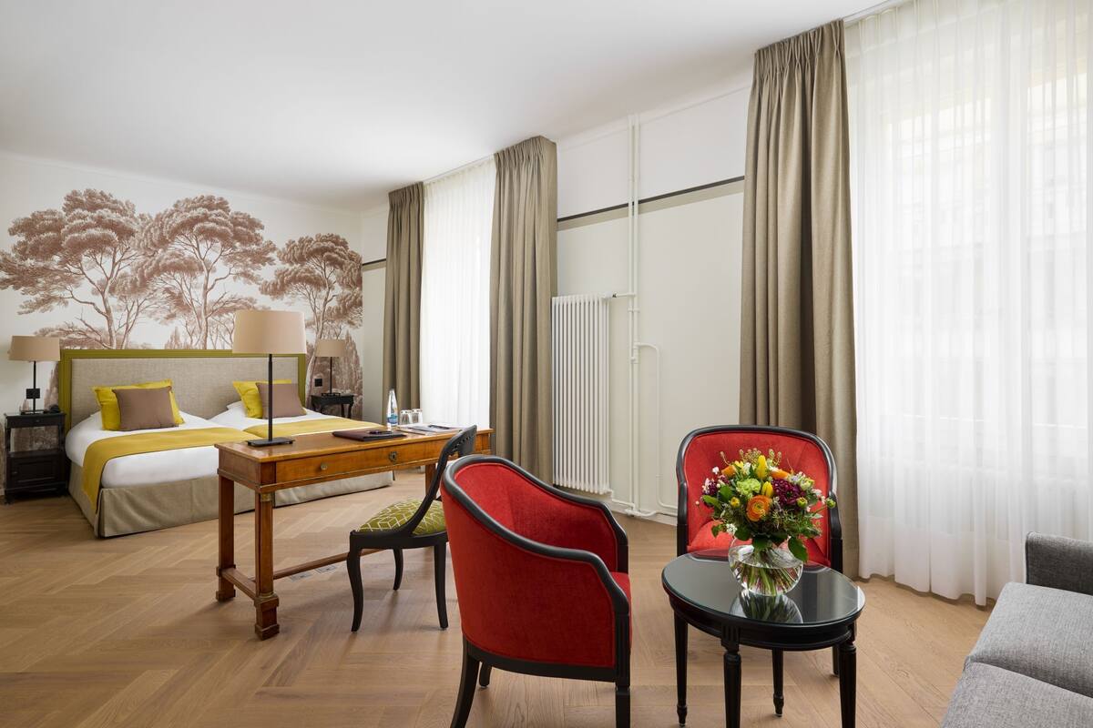 Habitación de hotel con cama, escritorio, silla y una mesita con un florero.