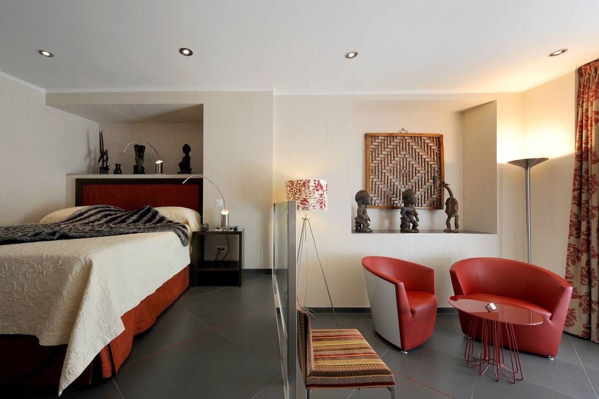 Una habitación de hotel moderna con cama, escritorio, silla, lámpara de pie y un adorno en la pared.