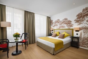 A hotel room with a bed, two chairs, a table with a vase of flowers, and a wall mural. - Hotel Victoria (Lausanne)