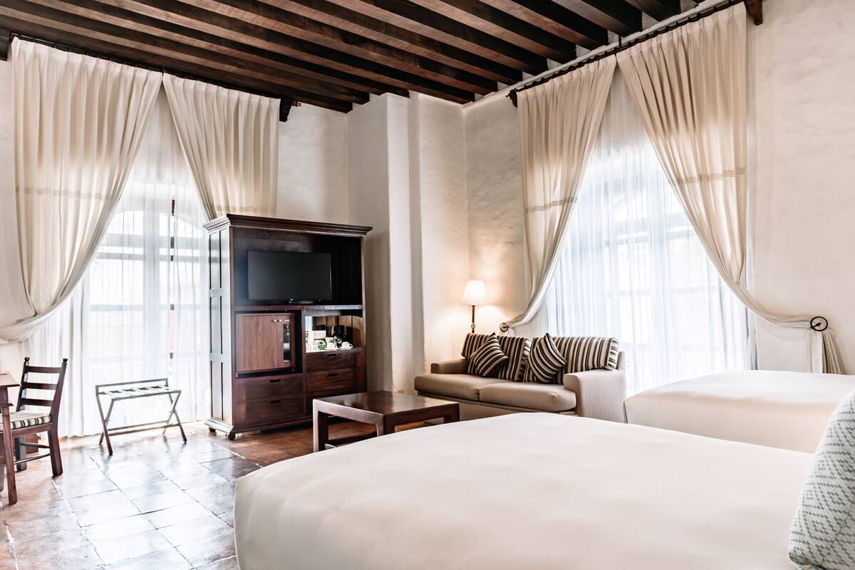 A hotel room with a large bed, a sofa, a TV, and a desk.