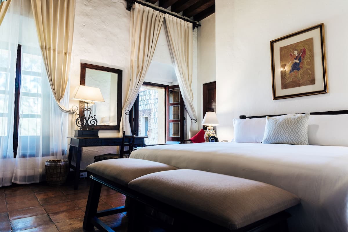 A hotel room with a large bed, two bedside tables, a chair, a desk, a lamp, and a framed picture on the wall.