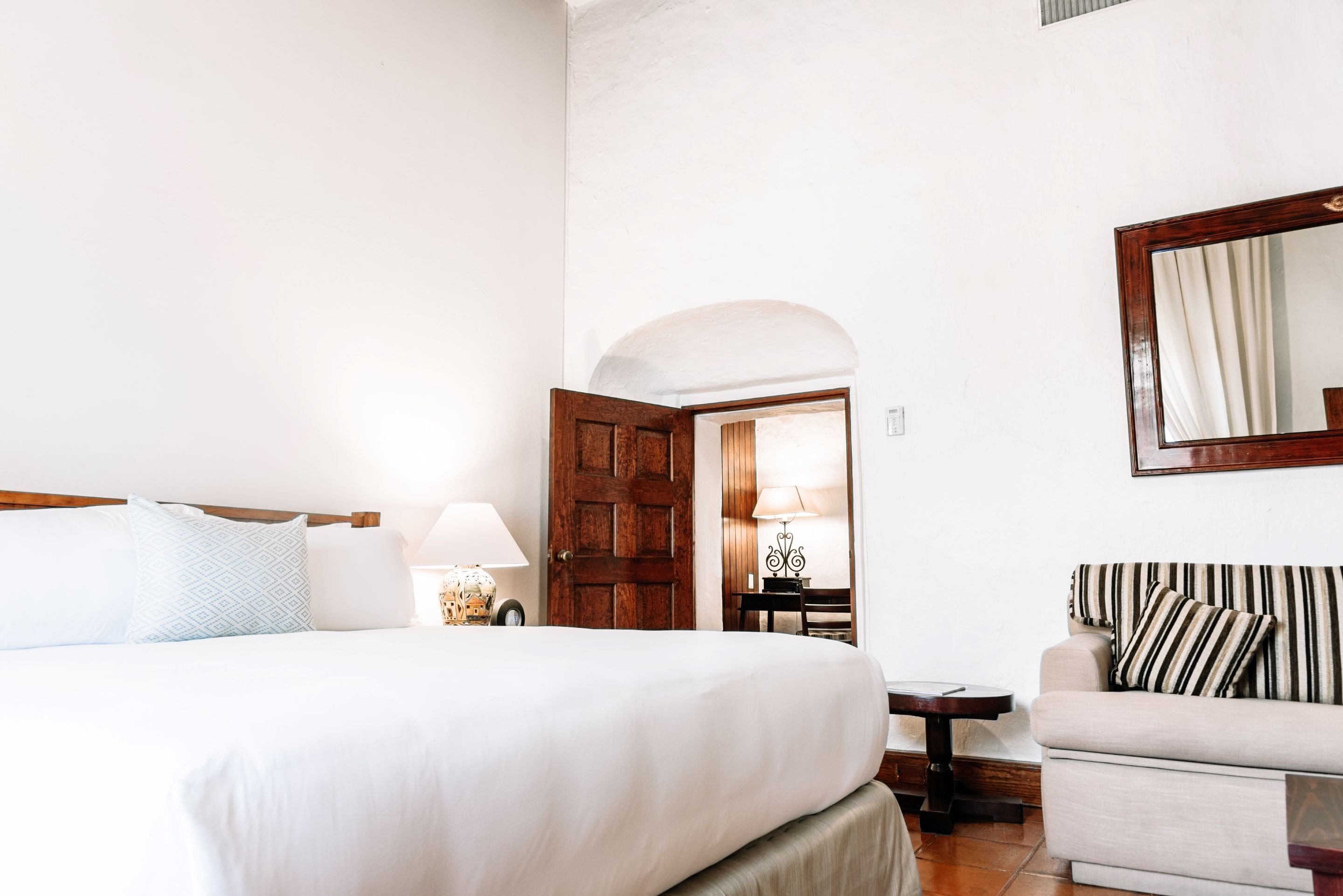 A hotel room with a bed, a sofa, a wooden door, and a mirror on the wall.