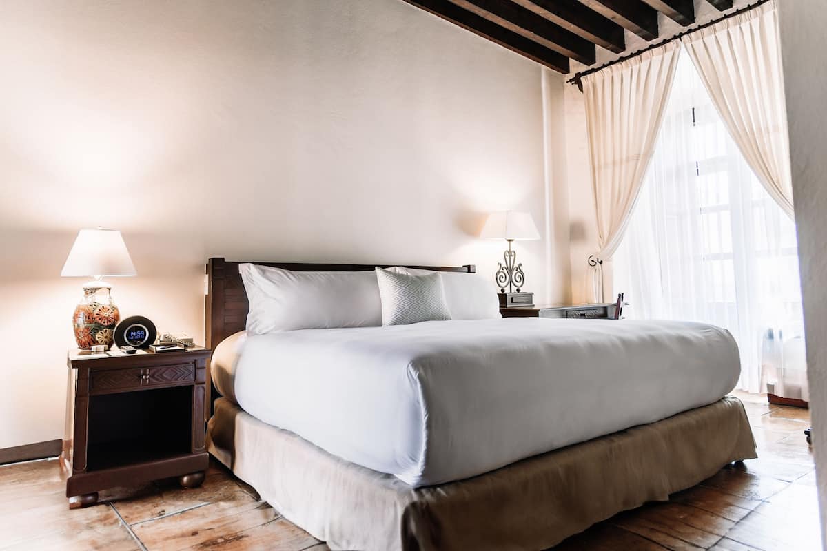 A neatly made bed with white linens, a wooden headboard, and a nightstand with a lamp and a decorative vase.
