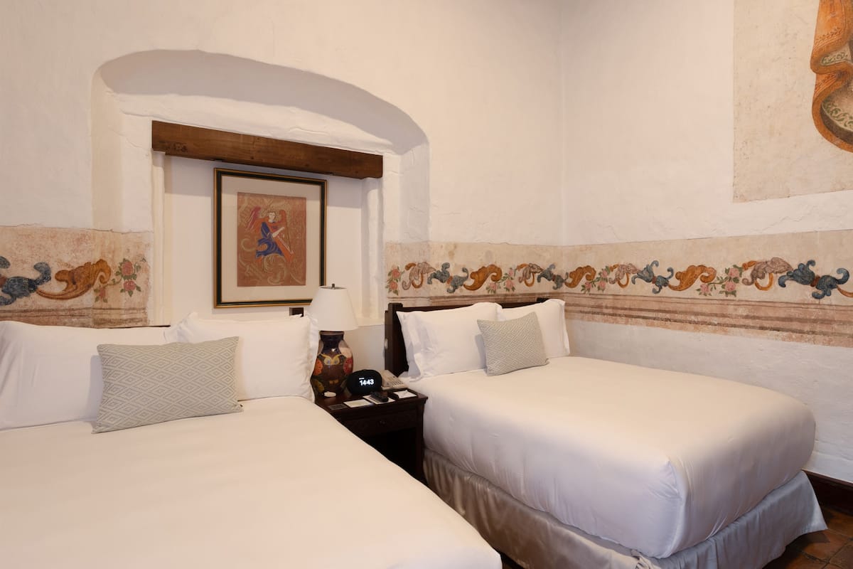 A hotel room with two beds, a nightstand, a lamp, and a painting on the wall.