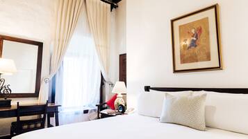 A hotel room with a bed, a desk, a chair, a lamp, a telephone, and a painting on the wall.