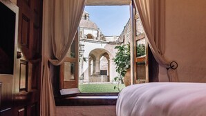 A room with a bed, curtains, and a view of an outdoor courtyard with arches and a building.