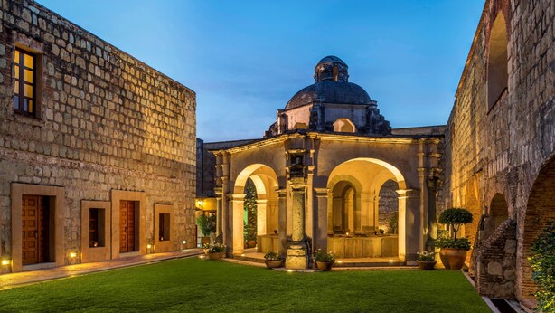 A courtyard with a central building featuring a dome and arches, surrounded by stone buildings.