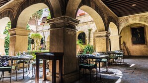 An outdoor patio with stone arches, tables, and chairs, surrounded by greenery.