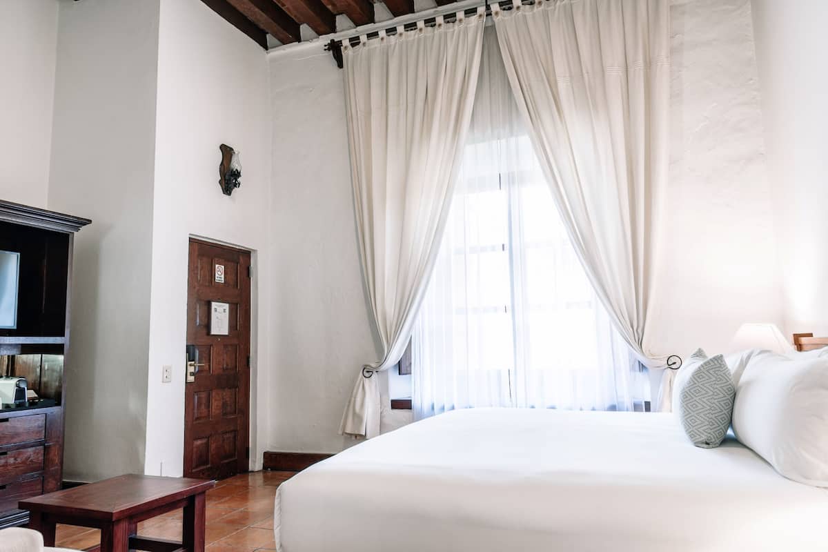 A bedroom with a large bed, a wooden table, a TV, and a door.