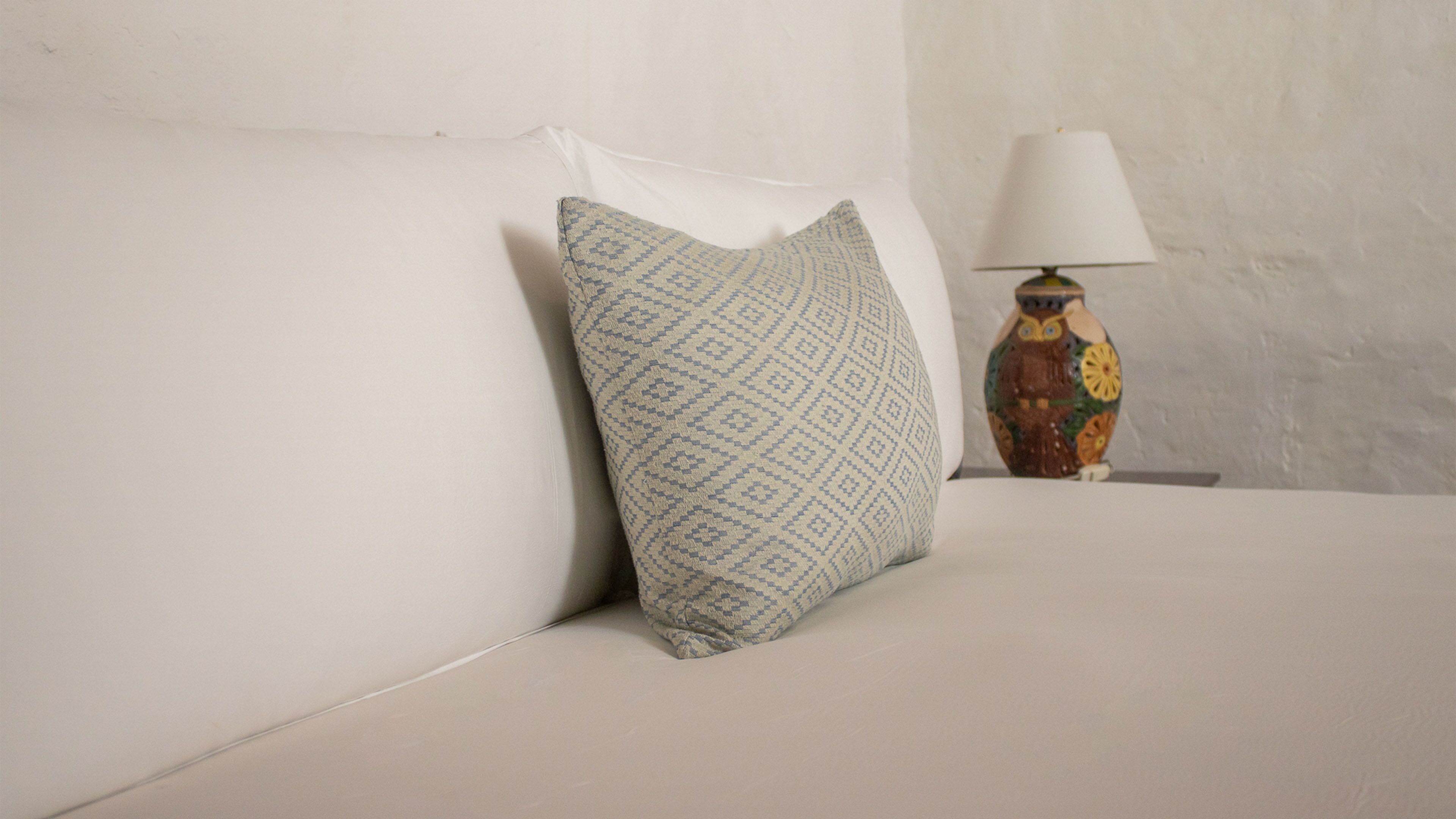 Una cama con un cojín estampado y una jarra decorativa en una mesita de noche.